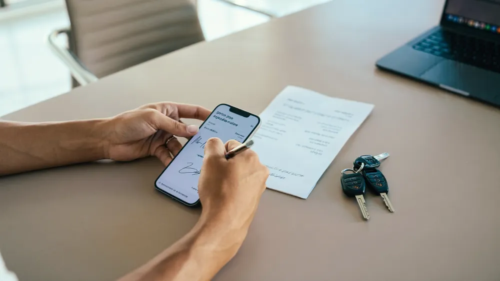 Assinatura eletrônica no celular ao lado da chave do carro e da nota fiscal na mesa da revenda